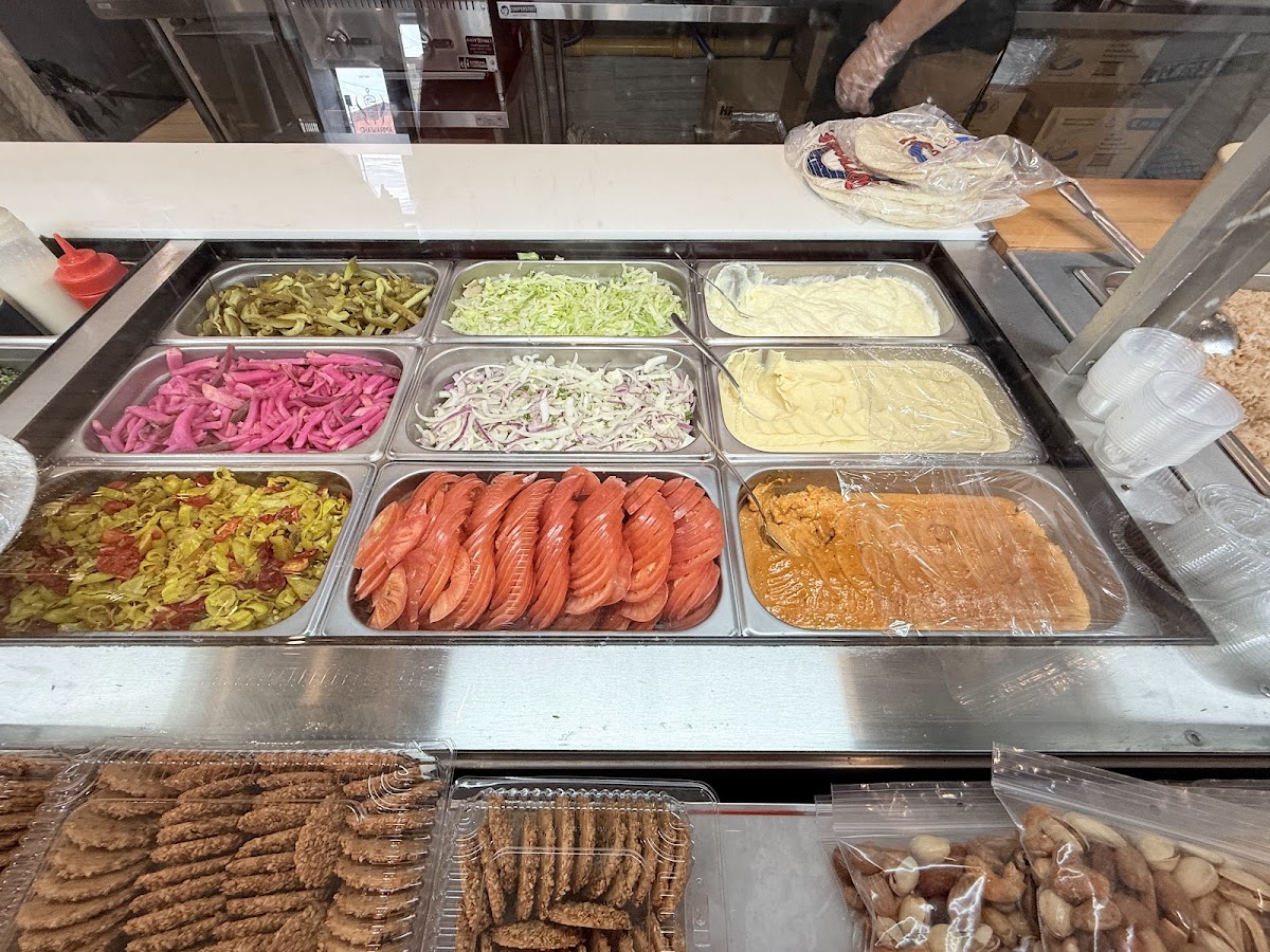 Close-up of the topping bar with pickled turnips, vegetables, sauces and stacked falafel