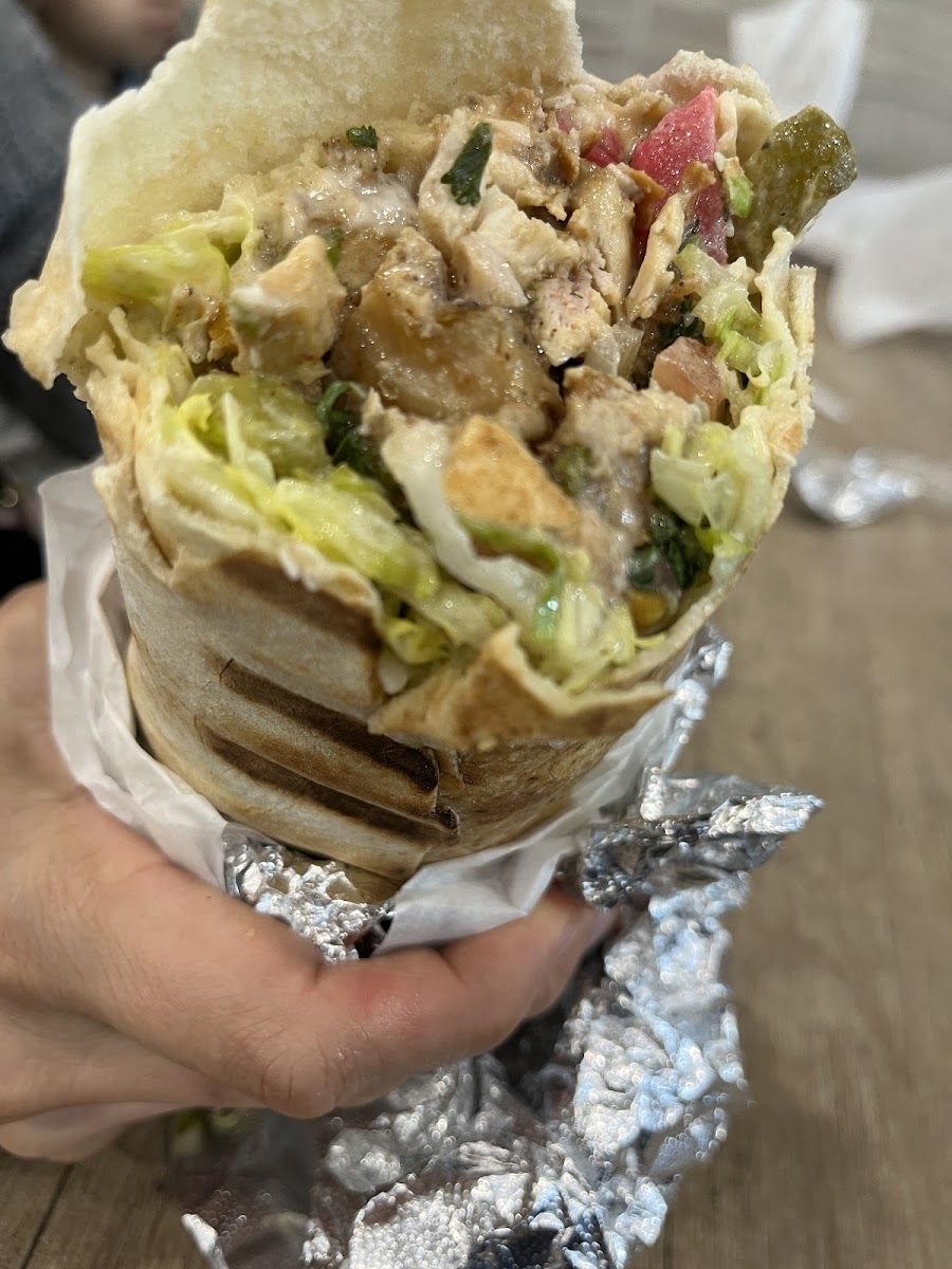 A hand holds a chicken shawarma wrap cut open showing chicken, lettuce and pickles